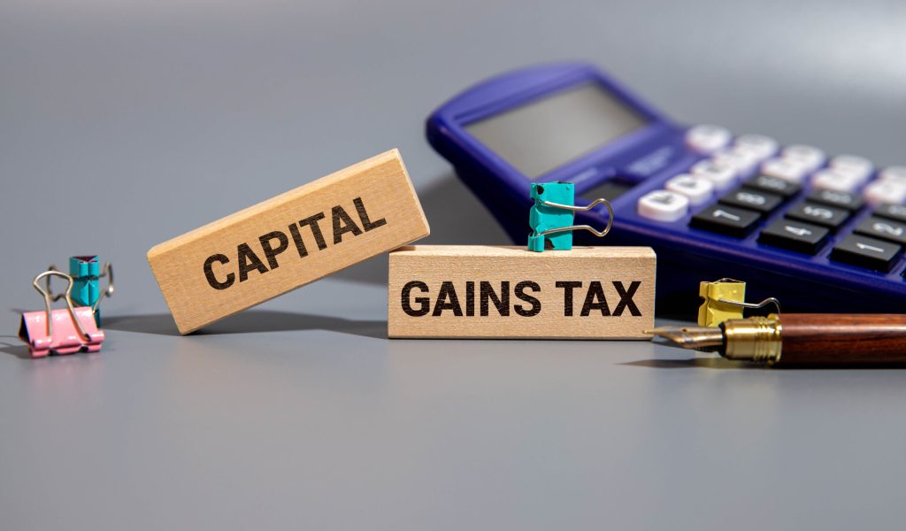 CAPITAL GAINS TAX word. Copy space. Concept word CAPITAL GAINS TAX on wooden blocks with diagram chart and office stuffs on the background. Business and financial concept.